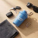 Shake Shot 4 oz blue mini shaker bottle on a wooden desk with car keys, earbuds and the shaker spring